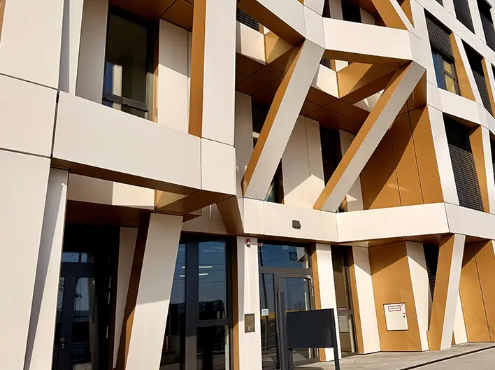 Detailed view of the entrance area of Brainfactory Bochum, featuring a distinctive façade structure, angled support elements, and modern architecture in white and gold tones.
